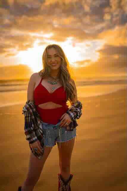 Smiling woman on sunset beach in casual outfit, summer evening scene.