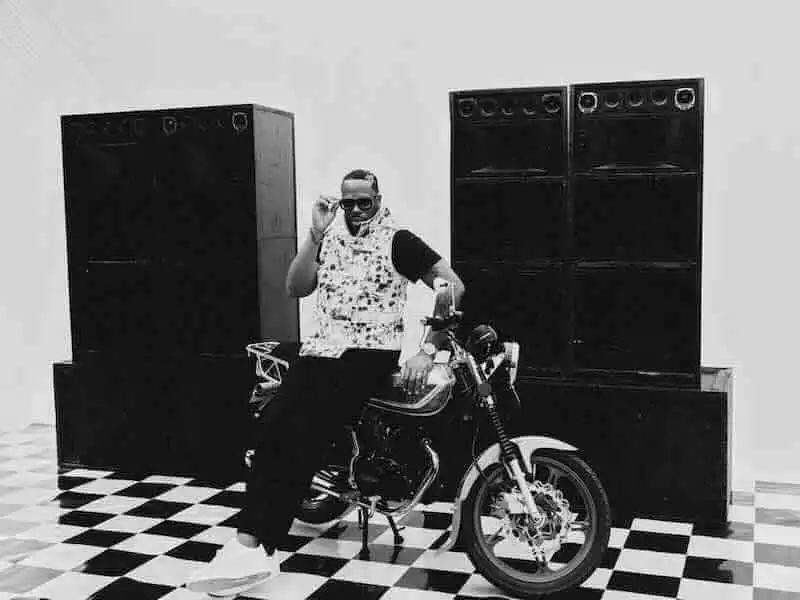 Stylish man posing on a motorcycle with speakers in an indoor setting.
