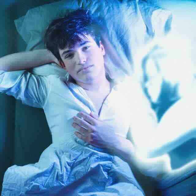 Young man lying on bed, soft lighting, contemplative mood, casual style.
