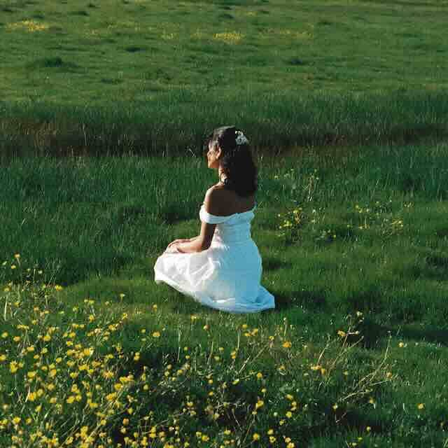 Peaceful woman sitting on lush green grass in a white dress with yellow wildflowers in a natural setting.