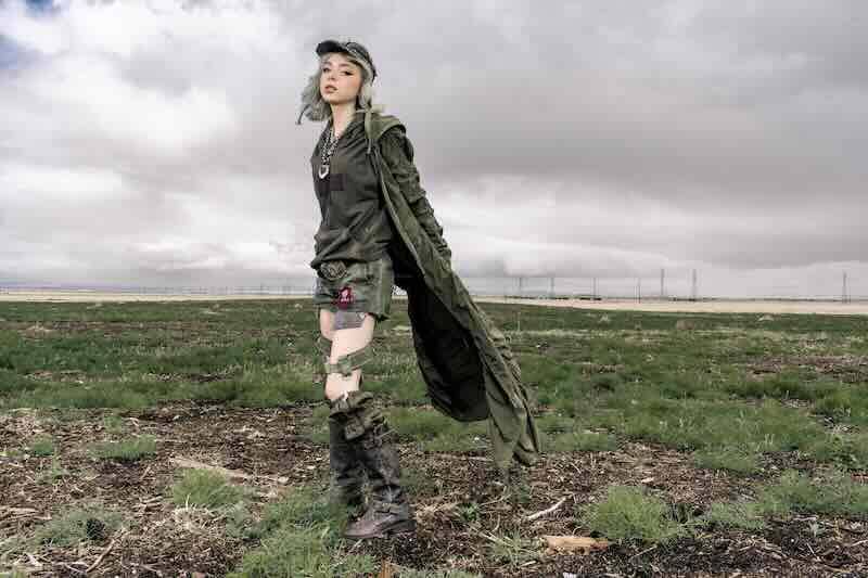 Young woman in distressed military-inspired outfit in a rugged outdoor landscape.
