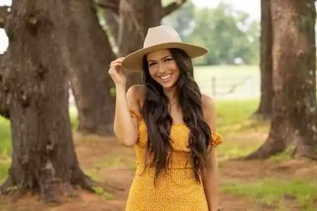 Beautiful woman outdoors wearing a yellow dress and wide-brim hat, enjoying nature and sunny weather.