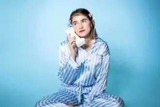 Young woman in pajamas talking on vintage phone against blue background.