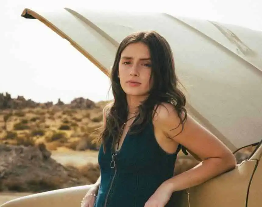 Young woman standing by car in desert landscape.