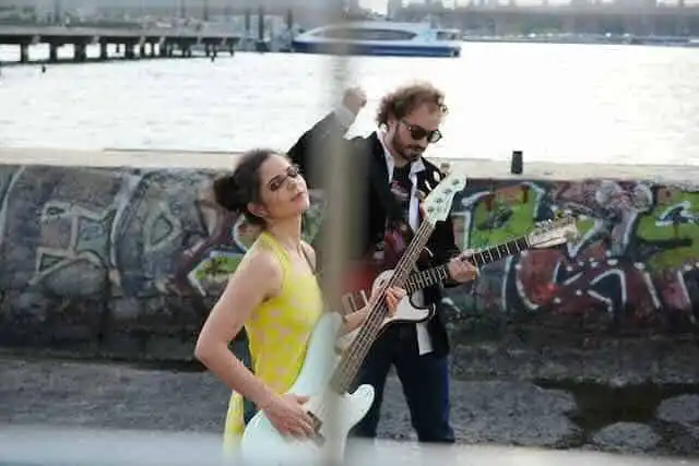 Stylish couple playing electric guitars outdoors near graffiti wall, capturing vibrant music scene.