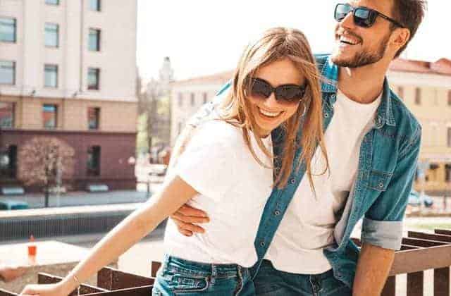 Happy couple in casual clothes, smiling and laughing outside on a city street.