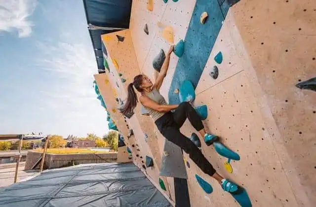 Female climber on outdoor rock wall, stretching for hold during workout.