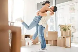 Happy couple embracing indoors with boxes and sunlight.