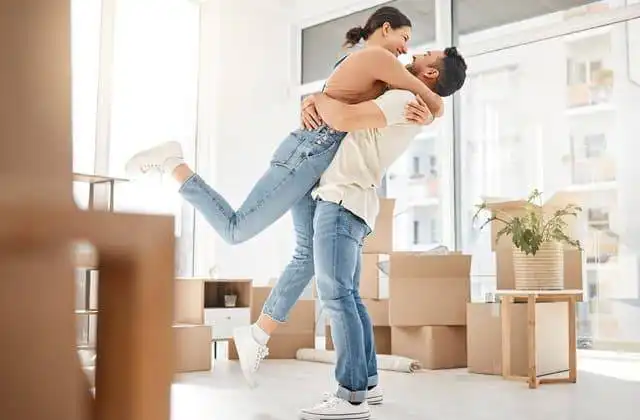 Happy couple embracing indoors with boxes and sunlight.