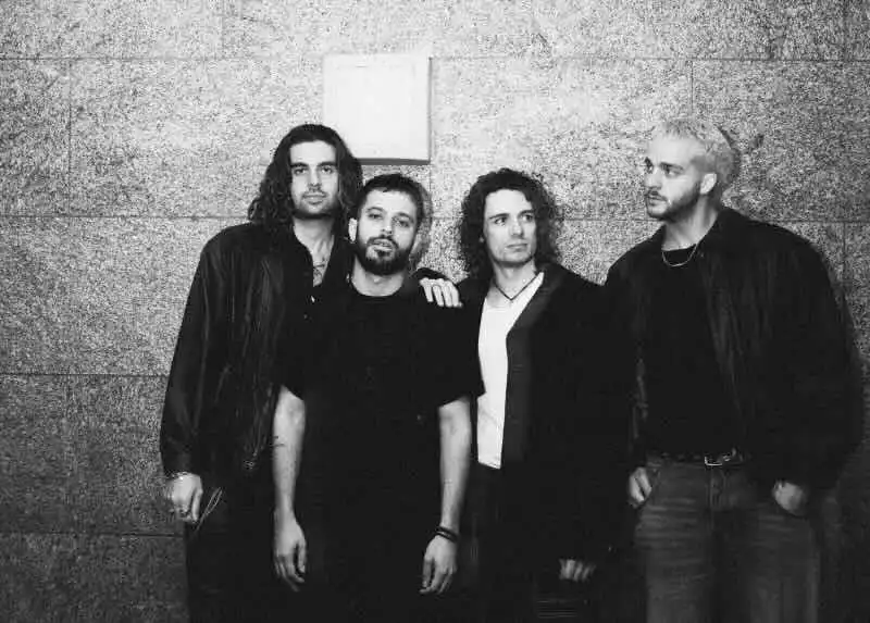 Alt text: Four male musicians standing against a textured wall, showcasing their unique styles.