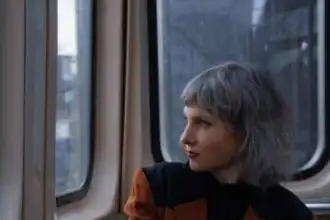 Trendy woman with gray hair gazing out train window, lifestyle, travel, urban fashion, divine magazine.