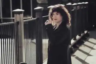 Candid portrait of a confident woman with curly hair standing by a black metal fence in urban setting.