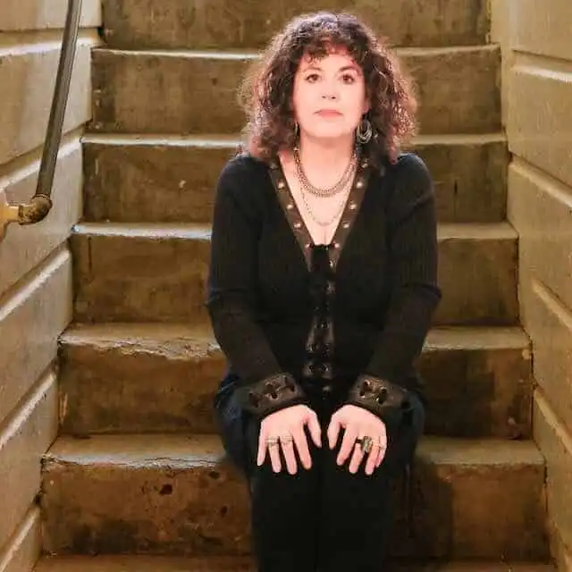 A woman with curly hair sitting on rustic wooden stairs, embodying strength and elegance in a black outfit.