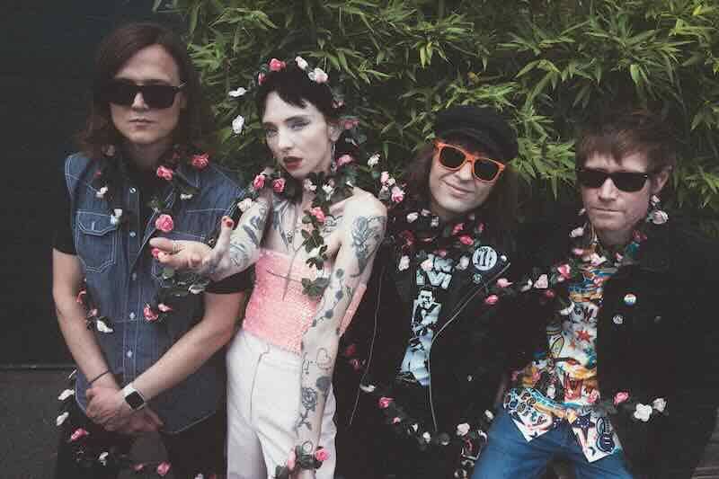 Alt text: Four people dressed in vibrant outfits with flowers, standing outdoors.