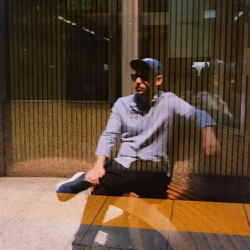 Young man relaxing on city bench with street reflections in glass.
