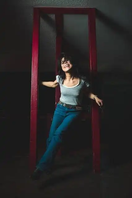 Happy woman smiling inside a red wooden frame, showcasing confidence and style.