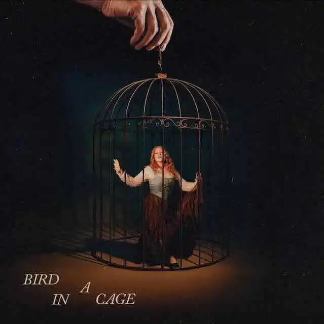 Elegant woman inside a vintage birdcage for artistic photoshoot.