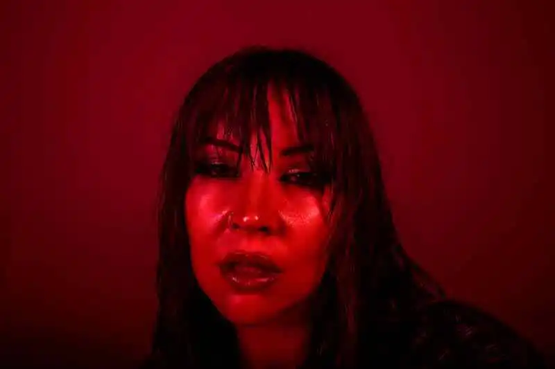 A striking woman with wet hair and bold makeup illuminated by intense red lighting, creating a dramatic and captivating atmosphere.