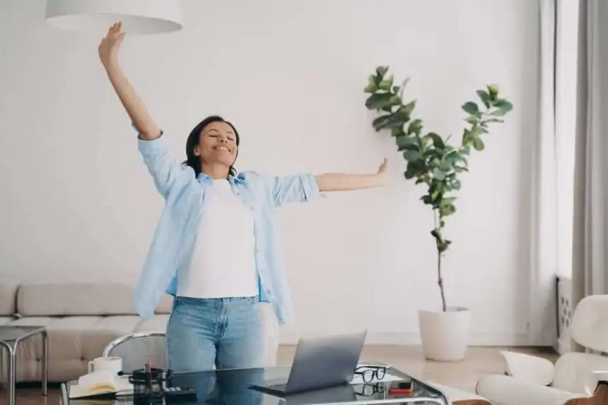 Happy woman enjoying morning stretch in a bright, modern home office.
