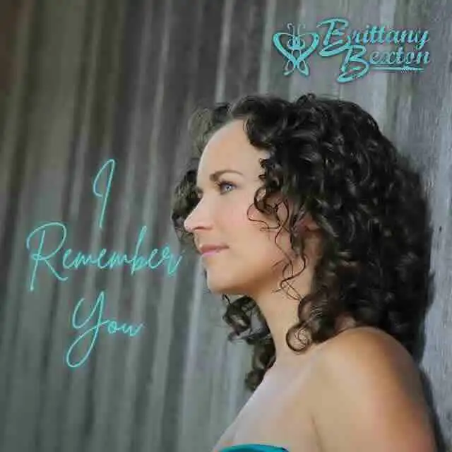 Beautiful woman with curly dark hair and a contemplative expression, standing by a dark wooden wall.