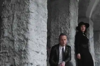Couple dressed in black and leather under stone archway.