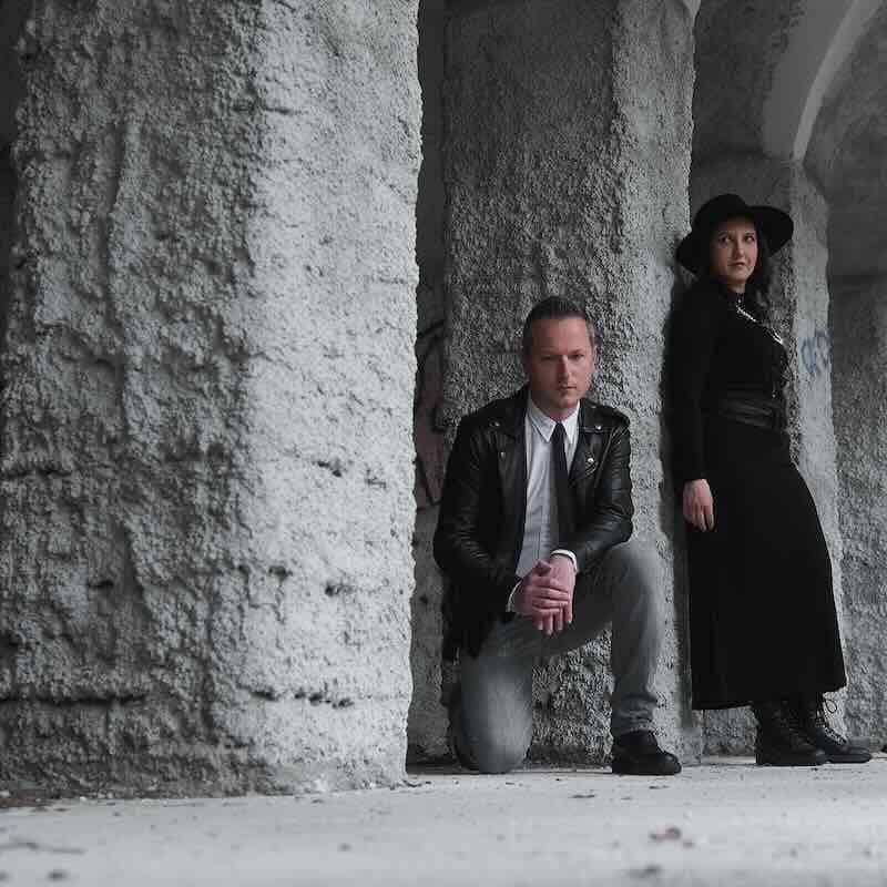 Couple dressed in black and leather under stone archway.