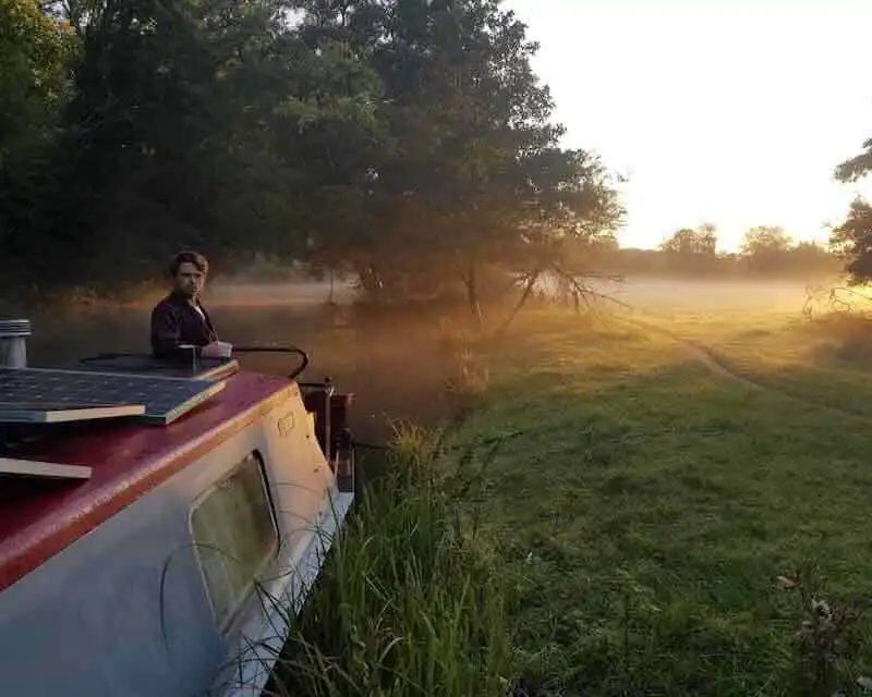 Beautiful sunset scene with a man on a boat beside a river at dawn, showcasing tranquility and nature for divine magazine readers.