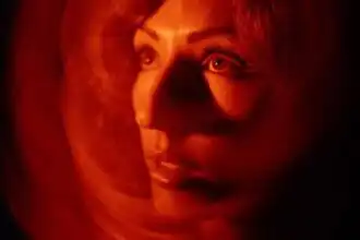 Close-up of a woman's face illuminated with warm red lighting, creating an artistic and mysterious atmosphere.