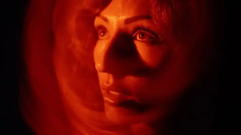 Close-up of a woman's face illuminated with warm red lighting, creating an artistic and mysterious atmosphere.
