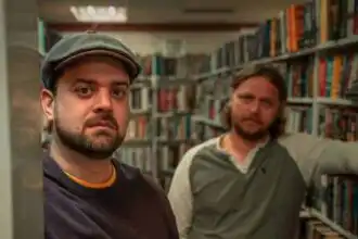 Two men standing in a lively bookstore aisle surrounded by colorful books.