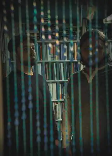Two men in a bookstore, one looking at the other through falling book pages, celebrating love and diversity.
