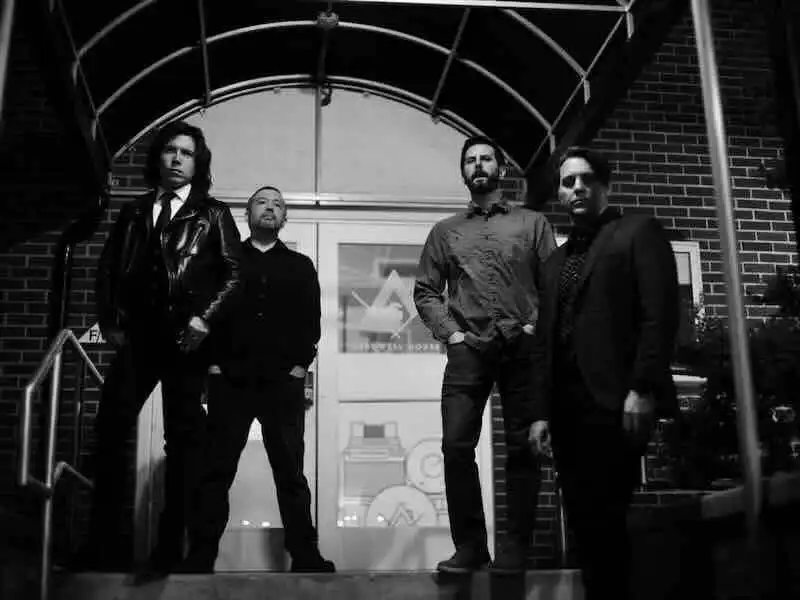 Alt text: Group of four men standing outside a building, posing confidently for a photo.