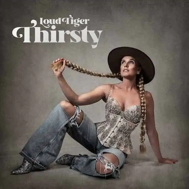 A woman with a long braided hair, large hat, and trendy outfit posing on the floor.