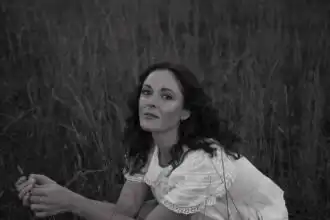 Woman sitting in tall grass, peaceful outdoor scene.