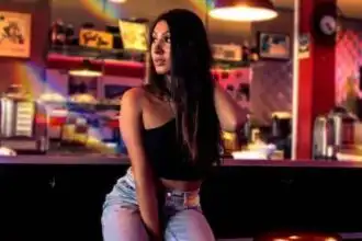 Young woman in trendy attire sitting in vibrant coffee shop, engaging in relaxed urban lifestyle.