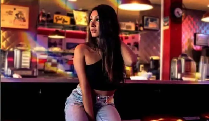 Young woman in trendy attire sitting in vibrant coffee shop, engaging in relaxed urban lifestyle.