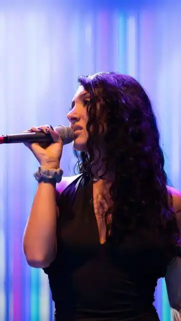Performer singing on stage with microphone at Divine Magazine event, vibrant colorful background.