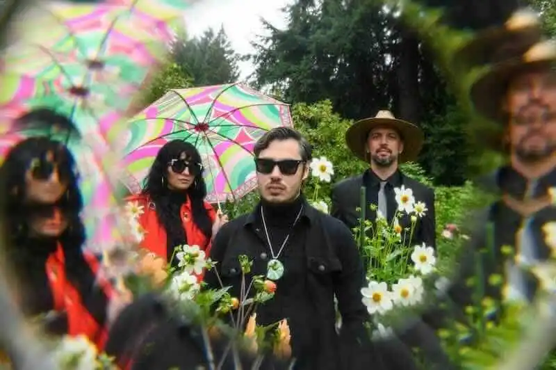 Vibrant outdoor photo featuring a diverse group of friends with umbrellas and flowers, capturing a lively and colorful garden scene.