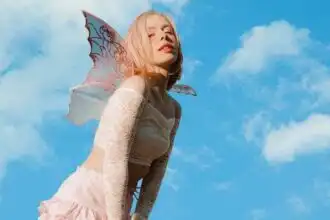 Elegant fairy with colorful wings under blue sky and clouds.
