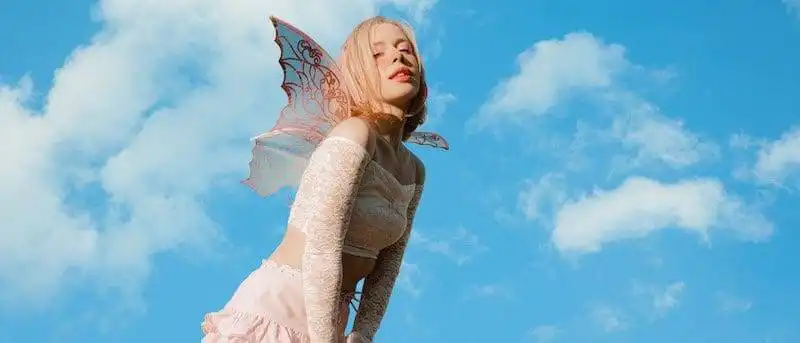 Elegant fairy with colorful wings under blue sky and clouds.