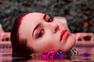 Beautiful woman relaxing in a pool with vibrant makeup, surrounded by colorful flowers.