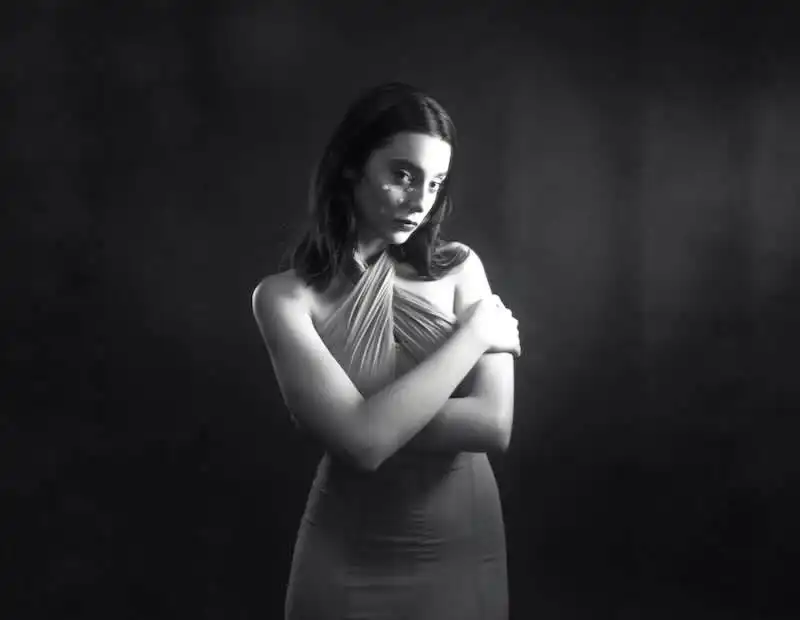 Elegant woman with crossed arms in a classic black-and-white photo, highlighting fashion and timeless beauty.