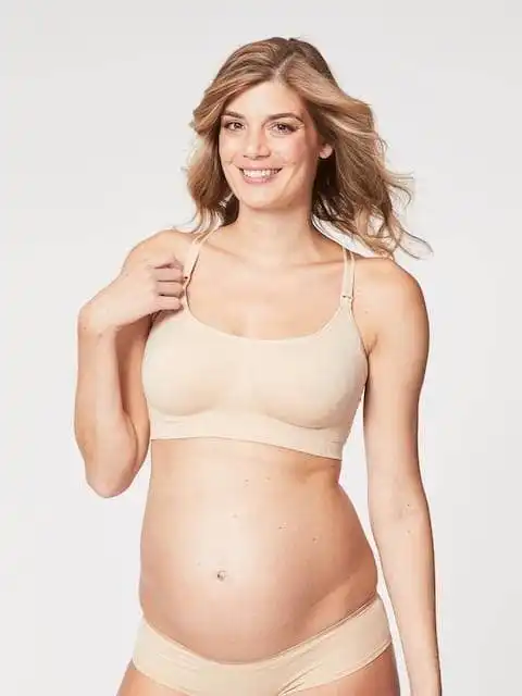 A smiling woman in beige underwear showcasing body positivity and confidence.
