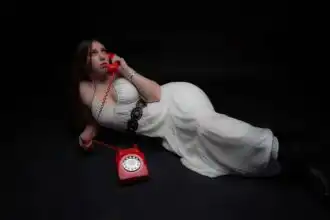 Girl lying on black background using vintage red rotary phone.