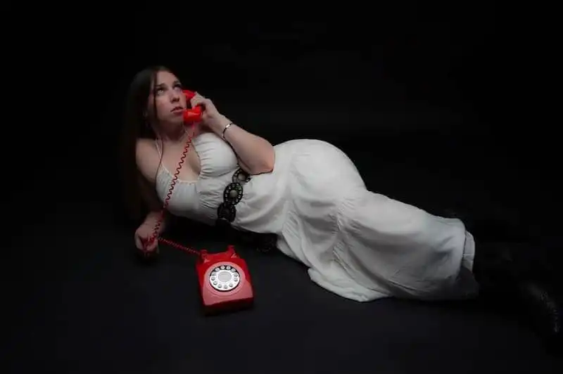 Girl lying on black background using vintage red rotary phone.