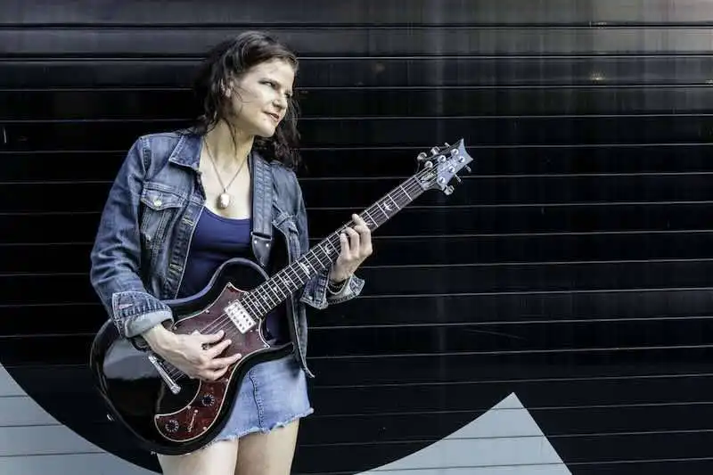 Young woman playing guitar outdoors in urban setting, casual denim outfit, expressive, vibrant lifestyle shot.