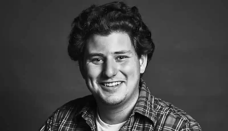 Smiling young man with curly hair in a plaid shirt, portrait in black and white.