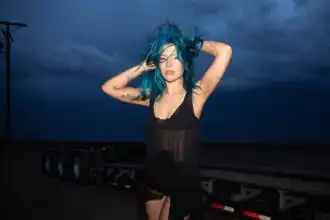 Vibrant blue-haired woman standing outdoors during stormy weather, showcasing fashion and personality.