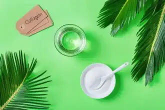 A glass of collagen drink, a spoonful of collagen powder in a bowl, and collagen tags surrounded by tropical leaves on a bright green background.