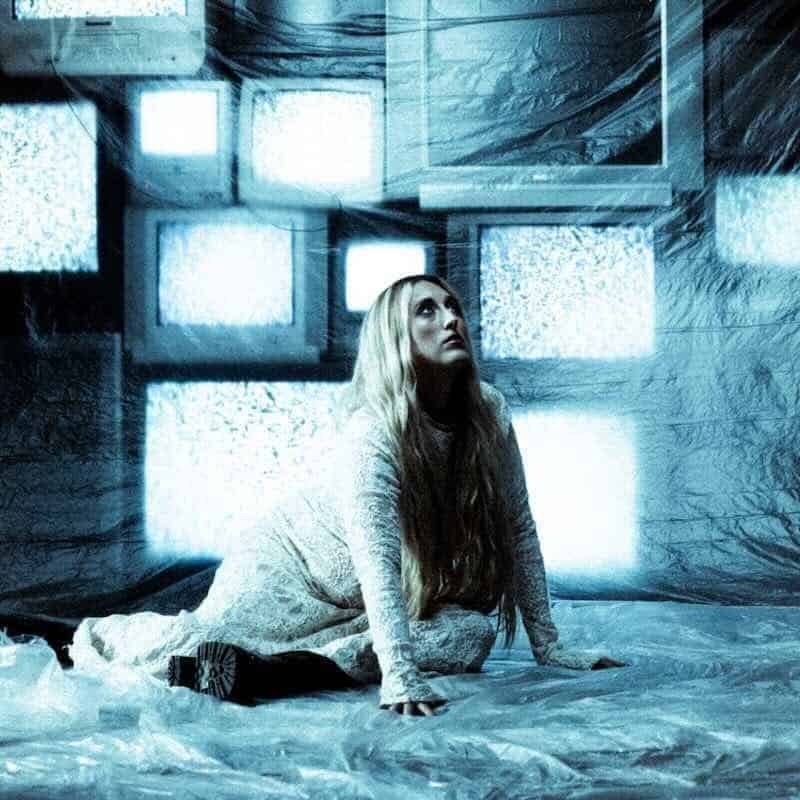 Woman on floor with glowing TVs behind her.